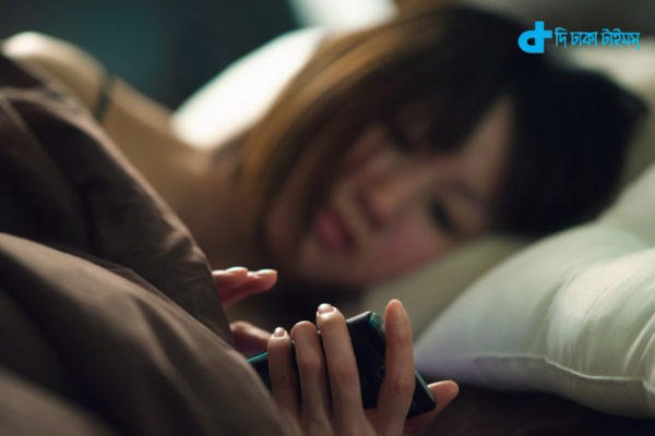 Young woman lying on side in bed operating smartphone